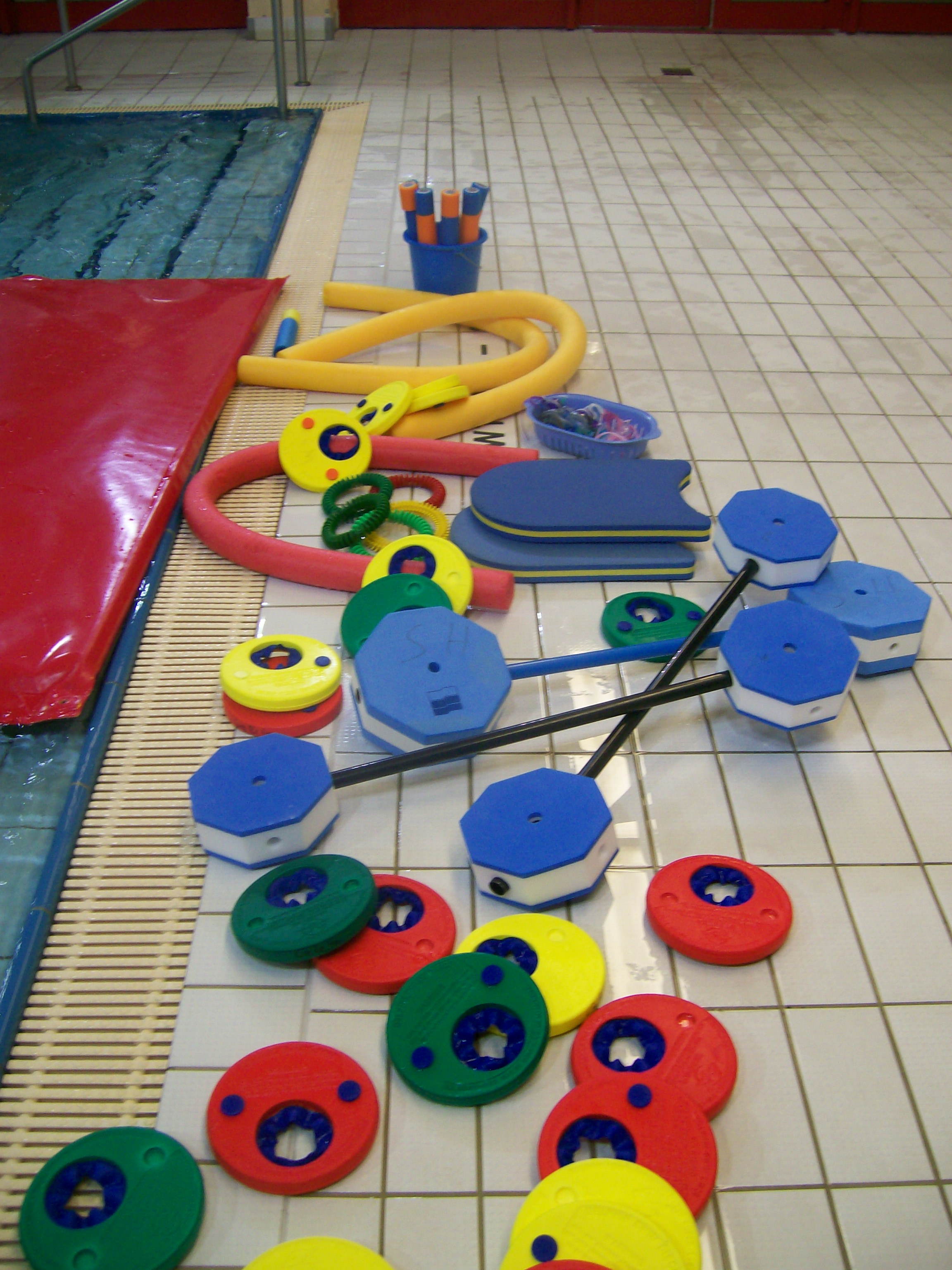Das Bild zeigt farbenfrohe Schwimmhilfen, die wild auf dem Boden der Schwimmhalle Neustadt liegen.